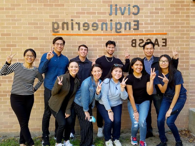 Students standing outside of civil engineering building with v's up smiling